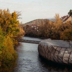 View of the Murinsel in Graz, nestled between colorful autumn trees along the river