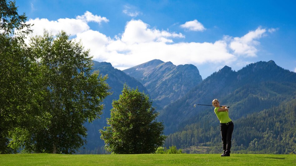 Golferin schlägt Golfball auf gemähten Rasen, Schönwetter vor einem Gebirge