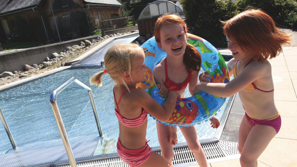 Drei Mädchen spielen mit einem Schwimmreifen beim Alpenbad in Mautern