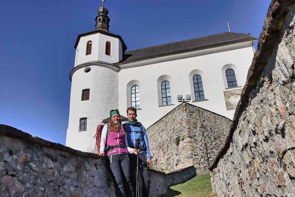 Ein Pärchen lächelt in die Kamera während sie vor der Wahlfahrtskirche stehen