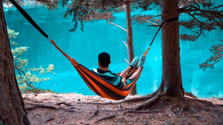 Ein Mann in einer zwischen zwei Bäumen gespannten Hängematte schaut auf den Grünen See