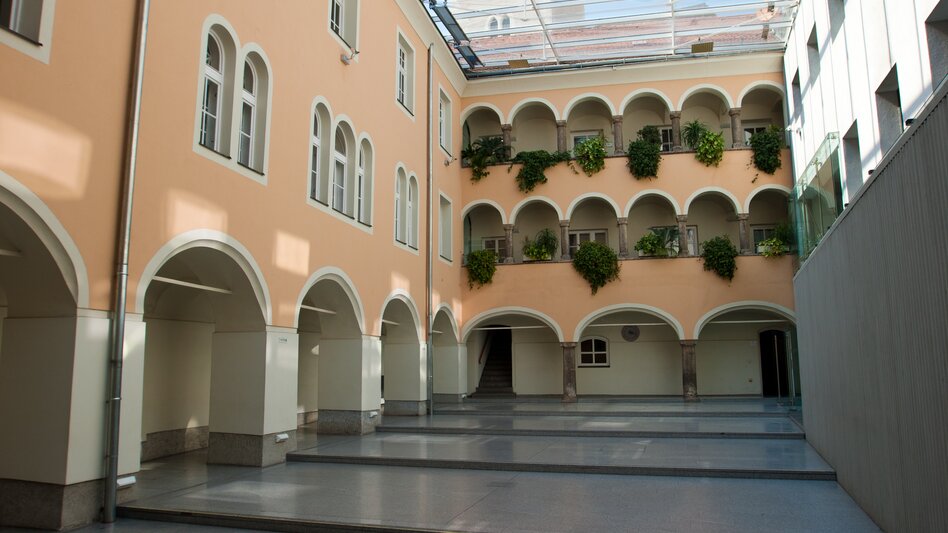 Ein Innenhof überdacht, durch die Glasfenster sieht man den Kirchturm