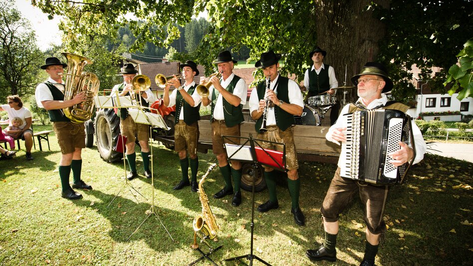 Eine Musikgruppe mit Blasinstrumenten spieln ein Stück, im Hintergrund sitzt ein Schlagzeugspieler in einem Traktorhänger