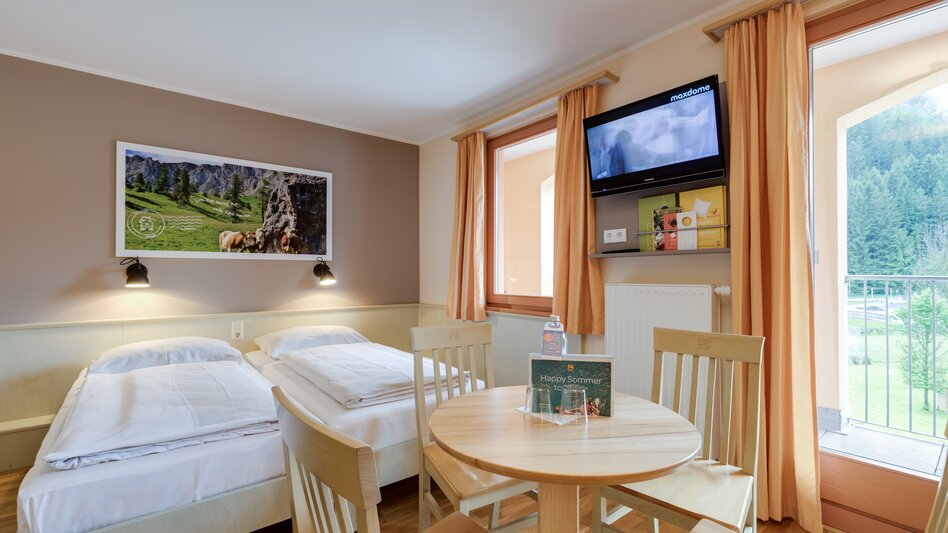 Ansicht eines Doppelzimmers mit einem runden Tisch und 4 Sesseln im JUFA Hotel Veitsch