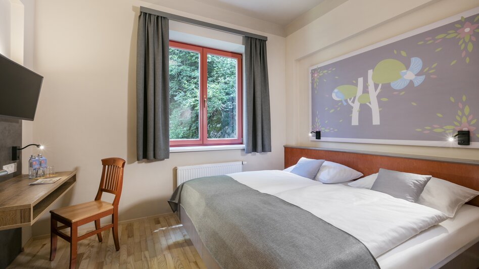 Zimmer im JUFA Hotel am Sigmundsberg mit einem Doppelbett, TV, Tisch und Sessel