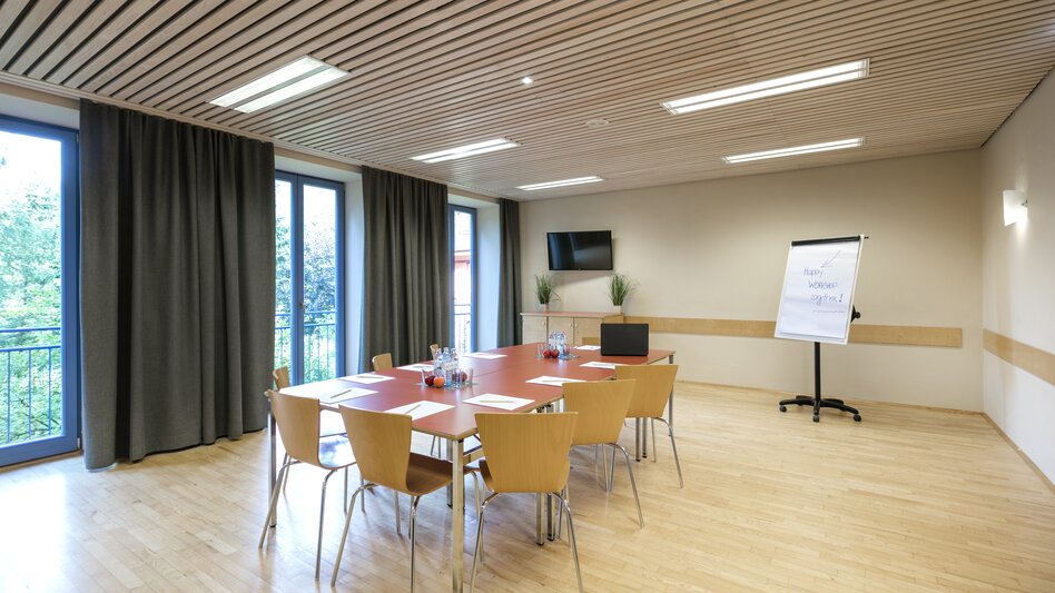 Ansicht eines Seminarraums im JUFA Hotel am Sigmundsberg mit Tisch, Sesseln und Flipchart
