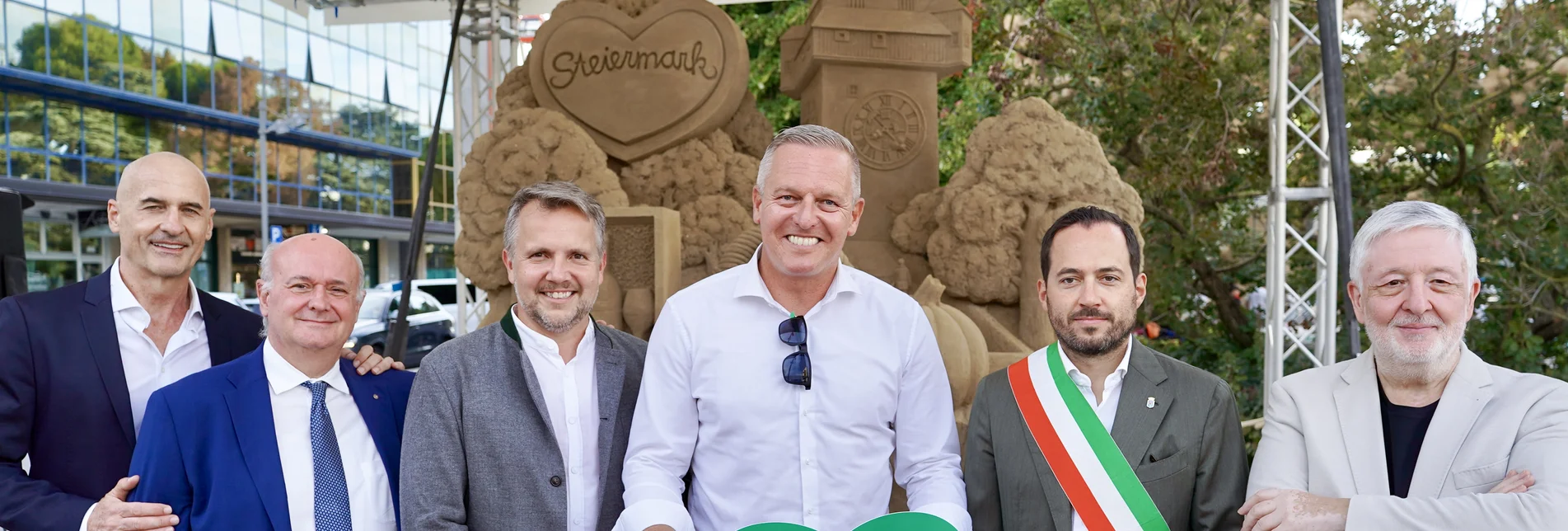 Sechs Personen Sandskulptur von links: Massimo Ambrosin (Kommunalpolitiker), Pierfrancesco Contarini (Präs. Hoteliersvereinigung AJA Jesolo), Michael Feiertag (GF STG), Landeshauptmann Mario Kunasek, Christofer De Zotti (Bürgermeister Jesolo), Angelo Faloppa (Hoteliersvereinigung) vor der Steiermark-Sandskulptur