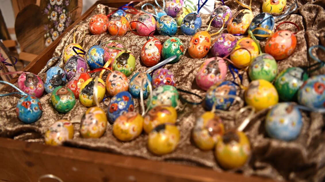 Bunte Sträuße aus Kräutern mit Schleifen in verschiedenen Farben liegen in einem Korb. Im Hintergrund sind weitere dekorierte Objekte auf einem Tisch sichtbar. | © KARLOO Entertainment