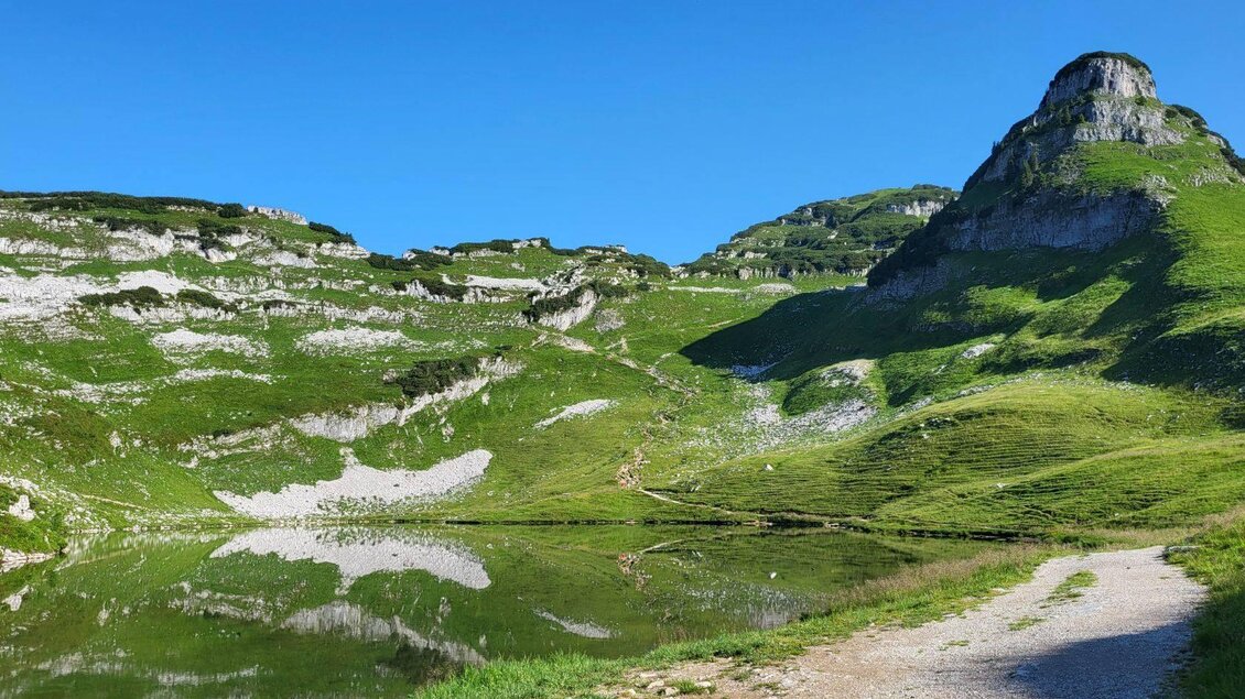 Eine ruhige alpine Landschaft mit einem klaren See und sanften Hügeln. Der Himmel ist blau und wolkenlos, perfekte Bedingungen für einen Ausblick in die Natur. | © Petra Kirchschlager