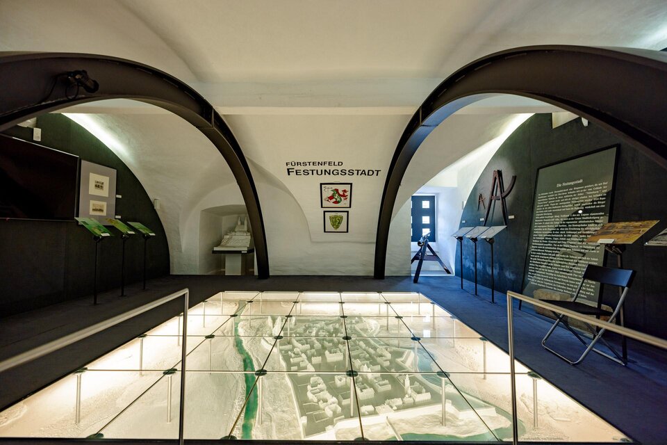 Ein Ausstellungsraum mit modernen Bögen und einem Diorama einer Festungsstadt. Die Wände sind mit Informationen und Erklärungen zur Geschichte der Stadt dekoriert. | © Stadtmarketing Fürstenfeld