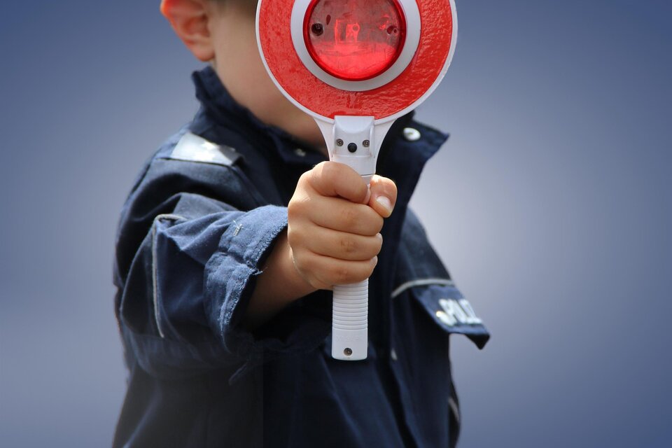 Ein Kind in einer Polizeiuniform hält eine rote Stoppschild. Der Hintergrund ist unscharf und hellblau. | © Pixbay