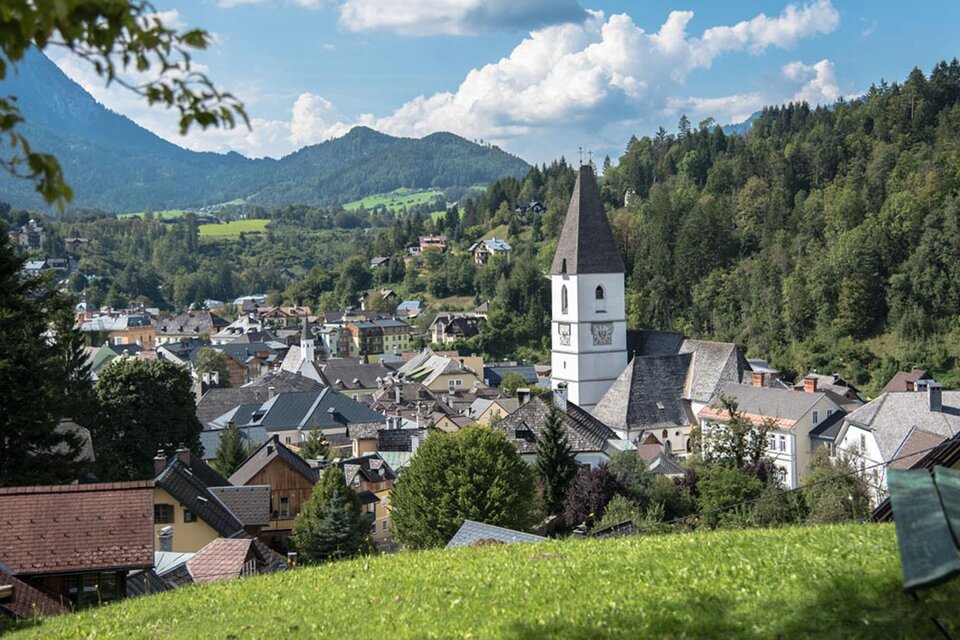 Die malerische Aussicht von der Tauscherin, einem Ausflugsziel in Bad Aussee. Das Bild zeigt den Blick von oben auf die Kurstadt Bad Aussee mit der Pfarrkirche und dem Stadtkern, umgeben von der grünen Landschaft und den Bergen des Ausseerlandes. Der Himmel ist blau und leicht von Wolken duchzogen. | © Herbert Sams
