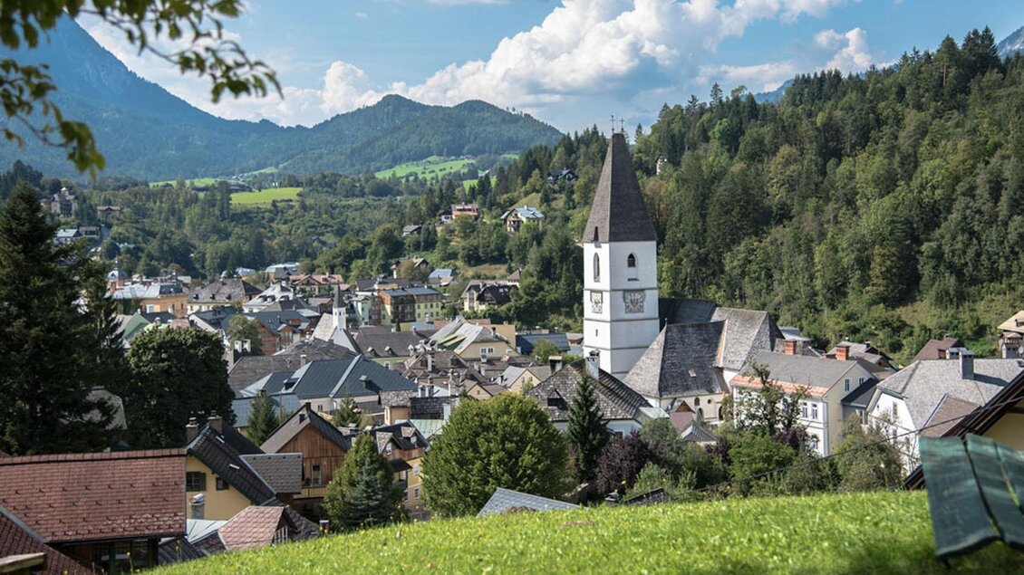 Die malerische Aussicht von der Tauscherin, einem Ausflugsziel in Bad Aussee. Das Bild zeigt den Blick von oben auf die Kurstadt Bad Aussee mit der Pfarrkirche und dem Stadtkern, umgeben von der grünen Landschaft und den Bergen des Ausseerlandes. Der Himmel ist blau und leicht von Wolken duchzogen. | © Herbert Sams