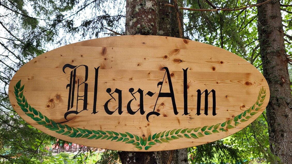 Ein hölzernes Schild mit der Aufschrift "Blaa-Alm". Es ist von Bäumen umgeben und vermittelt ein rustikales, einladendes Ambiente. | © Petra Kirchschlager