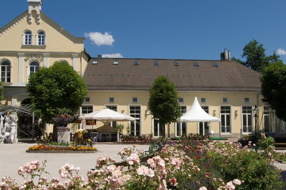 Eine elegante Gebäudeansicht mit einem schönen Garten. Bunte Blumen blühen vor dem Gebäude, und Sonnenschirme laden zum Verweilen ein. | © TVB Ausseerland Salzkammergut_Rastl