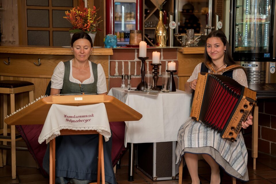 Zwei Frauen spielen traditionelle Musik in einer gemütlichen Atmosphäre. Die eine spielt auf einer Zither und die andere auf einem Akkordeon. | © Anita Fössl