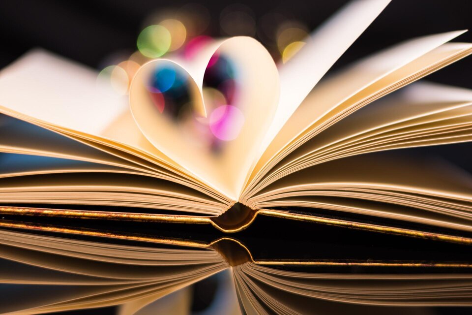 Ein aufgeschlagenes Buch mit einer Herzform aus den Seiten. Bunte Lichter leuchten im Hintergrund. | © Pixabay