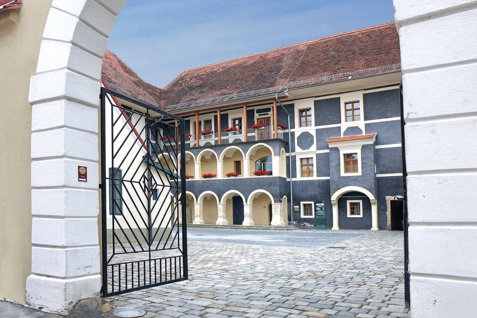 Innenhof des Museums Pfeilburg in Fürstenfeld, Steiermark: Historisches Gebäude mit Arkadengängen, blumengeschmückten Balkonen und gepflastertem Hof, stimmungsvolles Torbogen-Motiv, kulturelles Ausflugsziel in der Erlebnisregion Thermen- & Vulkanland. | © Museum Pfeilburg