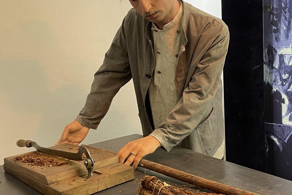Ein Mann arbeitet an einem Tisch mit einem Holzwerkzeug und zerkleinert Tabak. Neben ihm liegt ein Bündel Tabak. | © UMJ/E. Schlögl