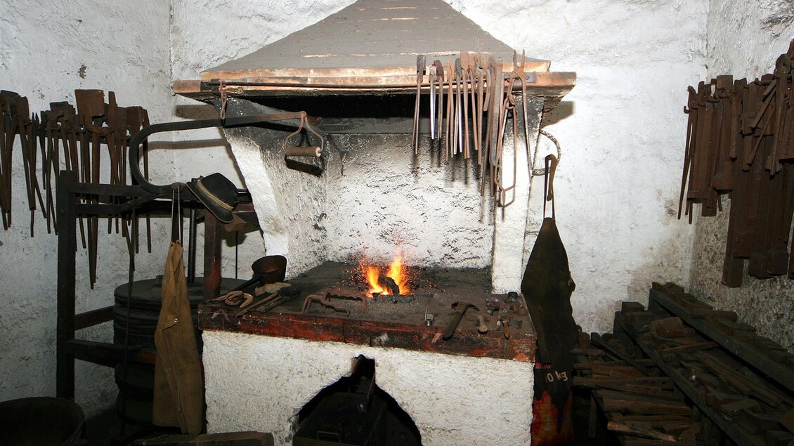 Eine traditionelle Schmiede mit einem offenen Feuer und vielen Werkzeugen. Die Wände sind aus Stein und die Einrichtung ist rustikal. | © Marktgemeinde Thörl