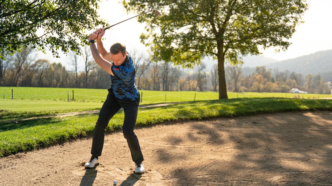 Ein Golfer spielt aus einem Bunker und bereitet sich auf den Schlag vor. Im Hintergrund sind Bäume und eine grüne Wiese zu sehen. | © Oststeiermark Tourismus