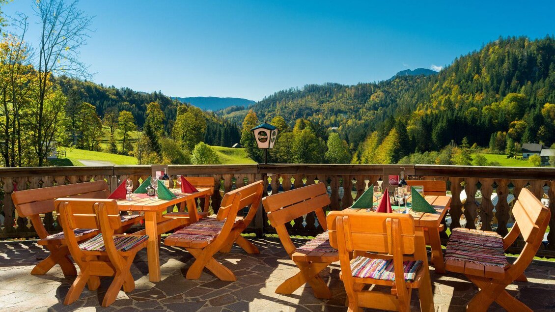 Ein einladender Außenbereich mit Holztischen und Stühlen. Im Hintergrund erstreckt sich eine schöne Berglandschaft mit buntem Laub. | © Gerhard Wolkersdorfer