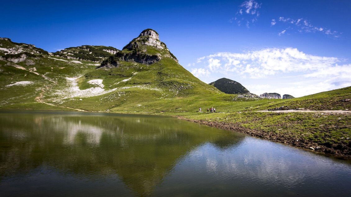 <p>Der malerische Augstsee umgeben von grünen Wiesen und dem markanten Atterkogel am Loser. Der klare Himmel spiegelt sich im ruhigen Wasser.</p> | © TVB Ausseerland - Salzkammergut-Tom Lamm