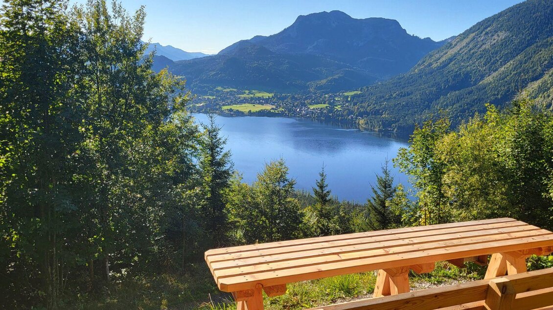 <p>Eine malerische Aussicht auf den klaren Altausseer See, umgeben von den Bergen und Wäldern des Ausseerlandes. Im Vordergrund steht die Holzbank, welche auch als Bürgermeisterbankerl bekannt ist.</p> | © TVB Ausseerland Salzkammergut