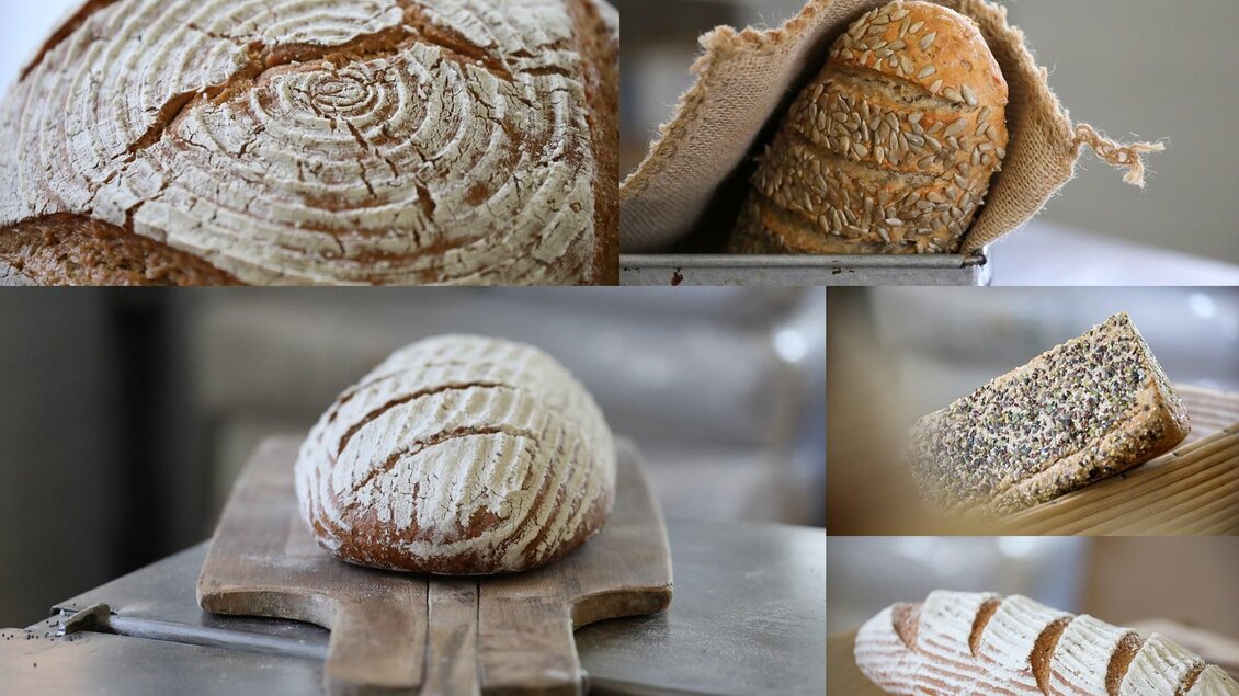 Verschiedene Brotsorten sind auf einem Holzbrett und in einem Behälter zu sehen. Das frische Brot hat eine rustikale, knusprige Kruste. | © GenussReich