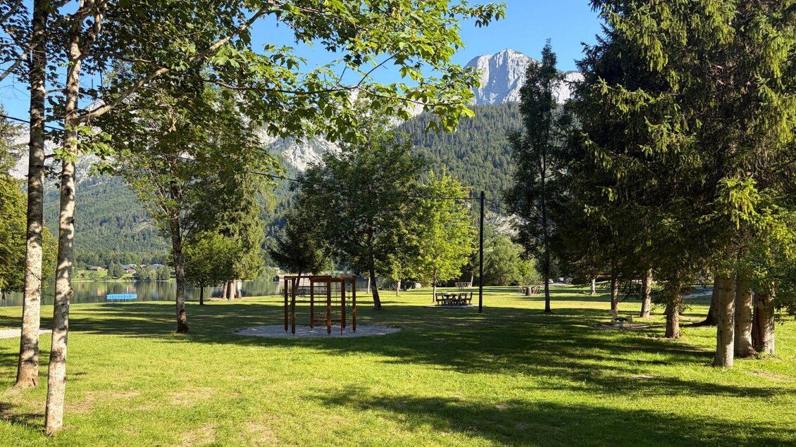 <p>Die großflächige Liegewiese beim Freizeitzentrum Gößl umgeben von zahlreichen schattenspendenden Bäumen. Im Hintergrund sind die Berge des Ausseerlandes und ein klarer Himmel zu sehen.</p> | © Tourismusverband Ausseerland