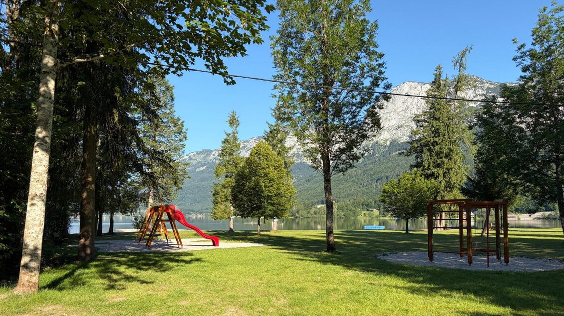 <p>Ein Spielplatz mit einer Rutsche und Schaukeln steht beim Freizetzentrum Gößl. Im Hintergrund sind Bäume und die Berge um den Grundlsee zu sehen.</p> | © Tourismusverband Ausseerland