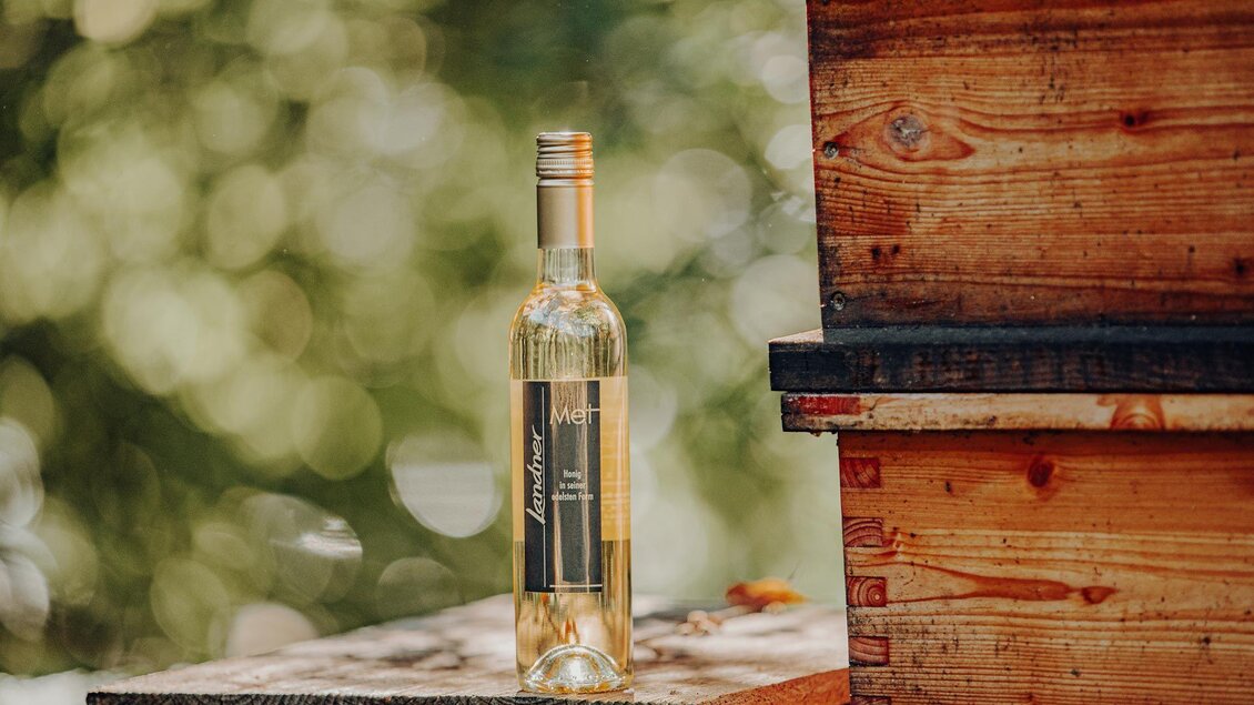 Eine Flasche Weißwein steht auf einem Holztisch. Im Hintergrund sind verschwommene grüne Bäume zu sehen. | © GenussReich