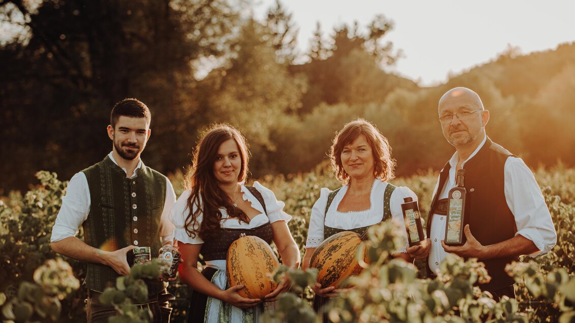 Eine Gruppe von vier Personen in traditioneller Kleidung steht in einem Weinberg bei Sonnenuntergang. Sie halten Melonen und Flaschen in den Händen. | © Freilichtmomente