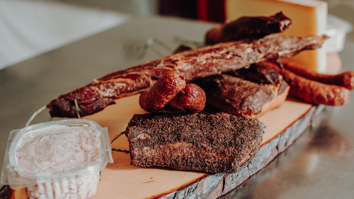 Eine Auswahl an verschiedenen Fleischsorten und Wurst auf einem Holzbrett. Dazu gibt es eine kleine Verpackung mit Aufstrich. | © GenussReich