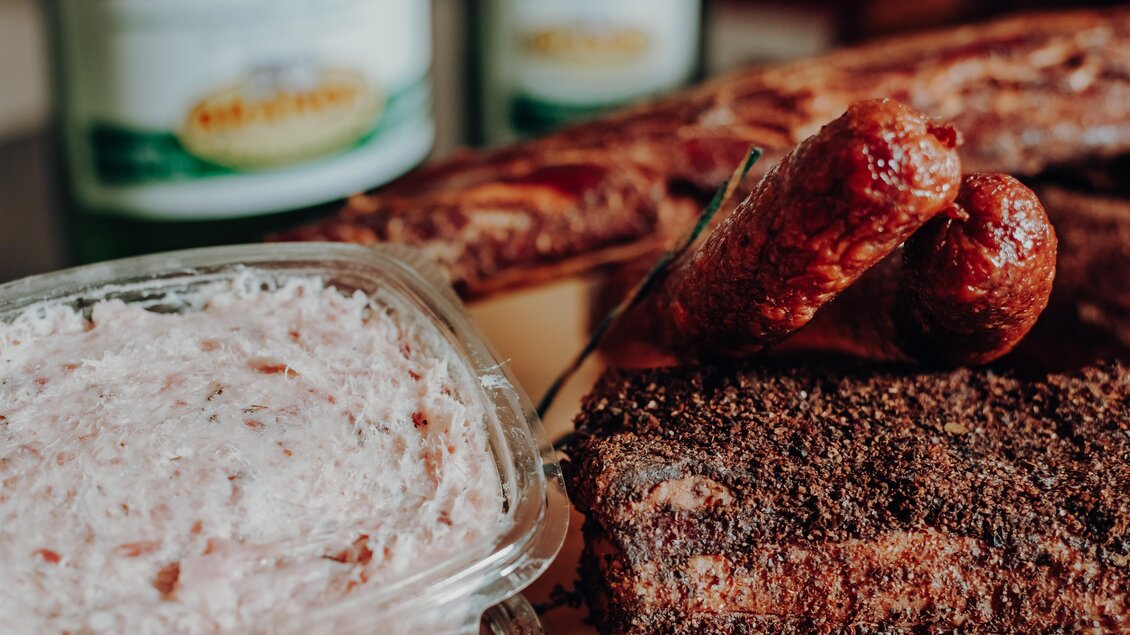 Eine Auswahl köstlicher Grillgerichte mit Rindfleisch, Wurst und einer cremigen Beilage. Im Hintergrund sind einige Flaschen Getränke zu sehen. | © GenussReich