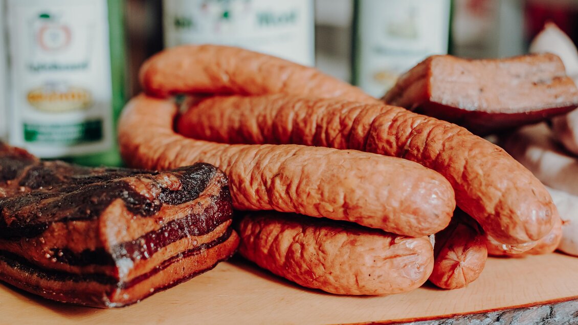 Eine Auswahl an Wurst und Fleisch auf einem Holzbrett. Im Hintergrund sind einige Flaschen Getränke sichtbar. | © GenussReich