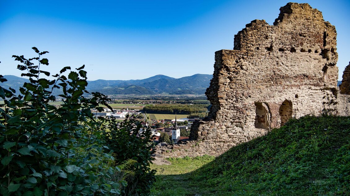 Eine alte Ruine steht auf einem Hügel mit Blick auf die umliegende Landschaft. Im Hintergrund sind sanfte Berge und ein klarer blauer Himmel zu sehen. | © Anita Fössl