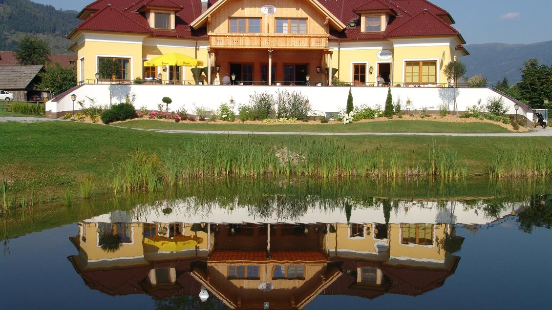 Ein schönes Haus mit einem roten Dach, umgeben von einem gepflegten Garten. Die Reflexion des Hauses ist im ruhigen Wasser eines Teiches zu sehen. | © Tourismusverband Murau
