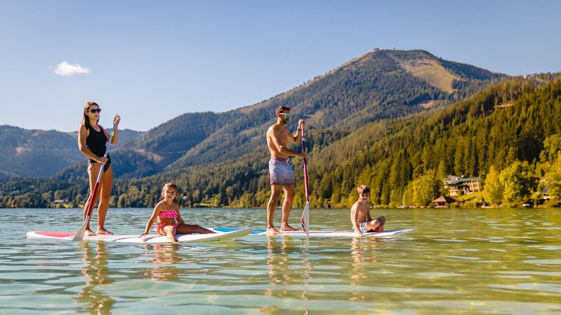 Eine Familie steht auf Stand-Up Paddle-Boards im ruhigen Wasser eines Sees. Im Hintergrund sind Berge und Bäume zu sehen. | © TV Hochsteiermark | Rudy Dellinger