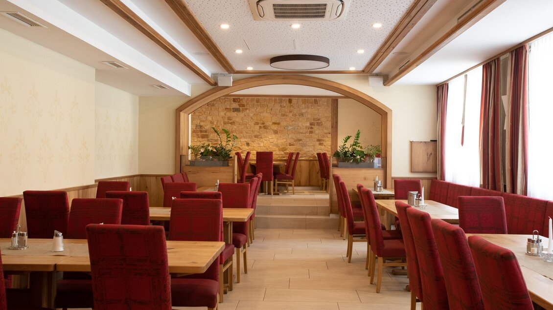 Ein gemütliches Restaurant mit roten Stühlen und Holztischen. Draußen strömt natürliches Licht durch die Fenster. | © achtungwirdrehen.com