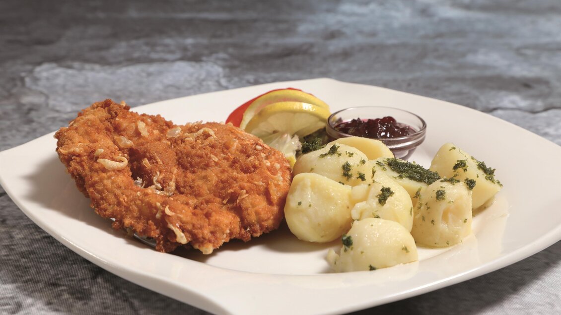 Ein Stück knuspriges Hähnchenfilet mit einer Beilage aus Kartoffeln. Dazu gibt es frische Äpfel und eine kleine Schüssel mit Preiselbeeren. | © Foto Freisinger