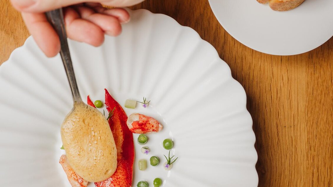 Ein elegantes Gericht auf einem weißen Teller mit einer Zubereitung von Meeresfrüchten und frischen Erbsen. Im Hintergrund liegt eine weitere Portion auf einem kleinen Teller.