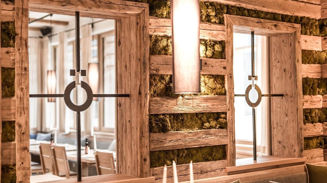Der Gastraum im Restaurant hat ein rustikales Interieur mit Holzverkleidung und grünem Wandbewuchs als Dekoration. Zwei Fenster lassen viel Licht herein und reflektieren den hellen Raum.</p> | © Genuss am See-Dieter Sajovic
