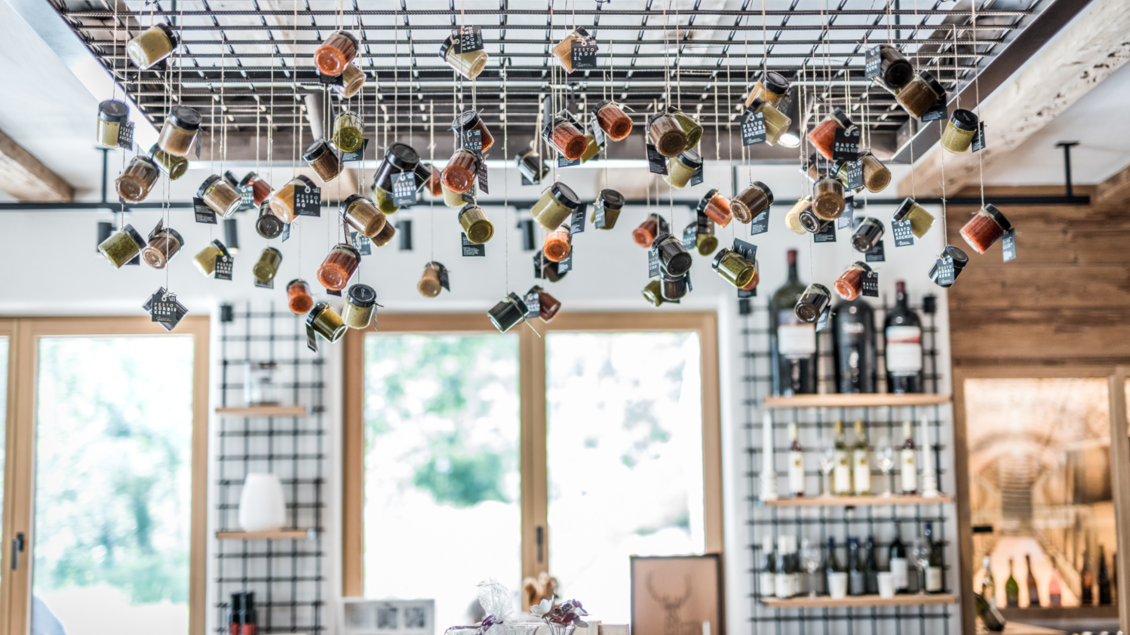 Der Genussladen im Untergeschoss vom Restaurant mit bunten, hängenden Gewürzgläsern. Im Hintergrund sind Regale mit Weinflaschen sichtbar. | © Genuss am See