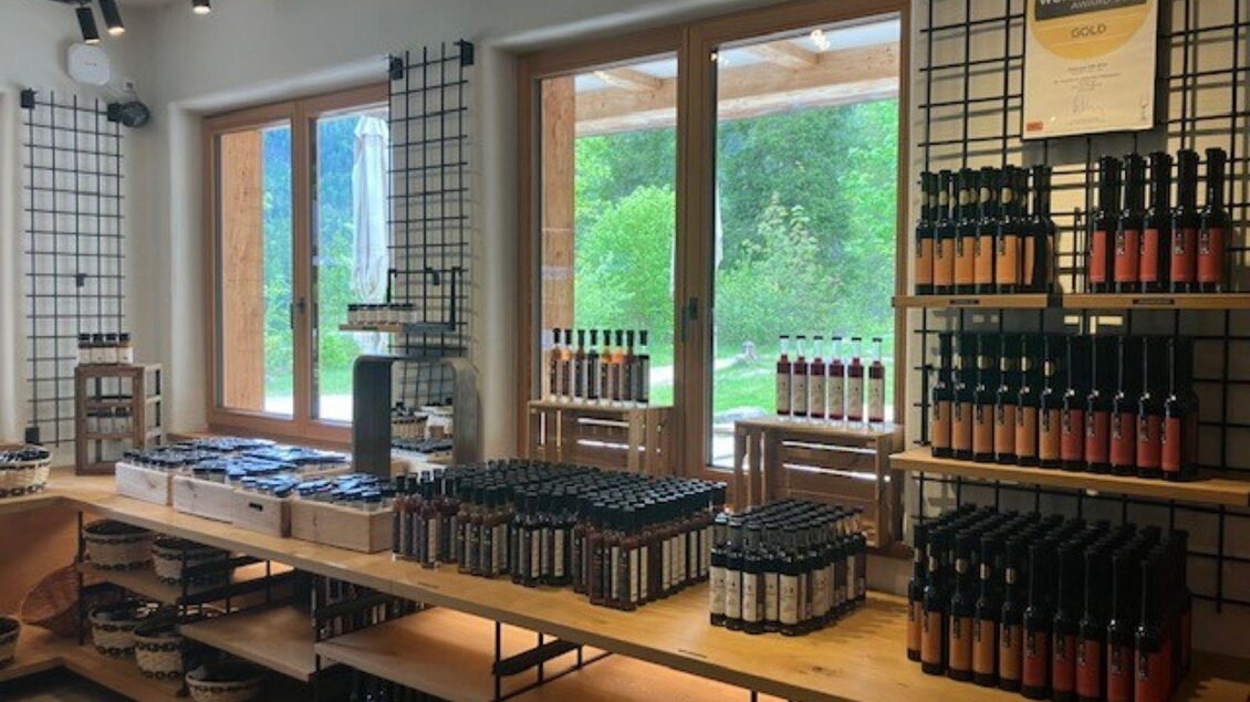 Der Verkaufsraum des Genussladens ist ausgestattet mit Regalen voller Flaschen und Produkten, wie zum Beispiel Grillsaucen, Chutneys, Pasta und Schokolade. Große Fenster bieten einen Blick auf die grüne Umgebung rund um den Ödensee. | © TVB Ausseerland Salzkammergut (c) Heike Temmel