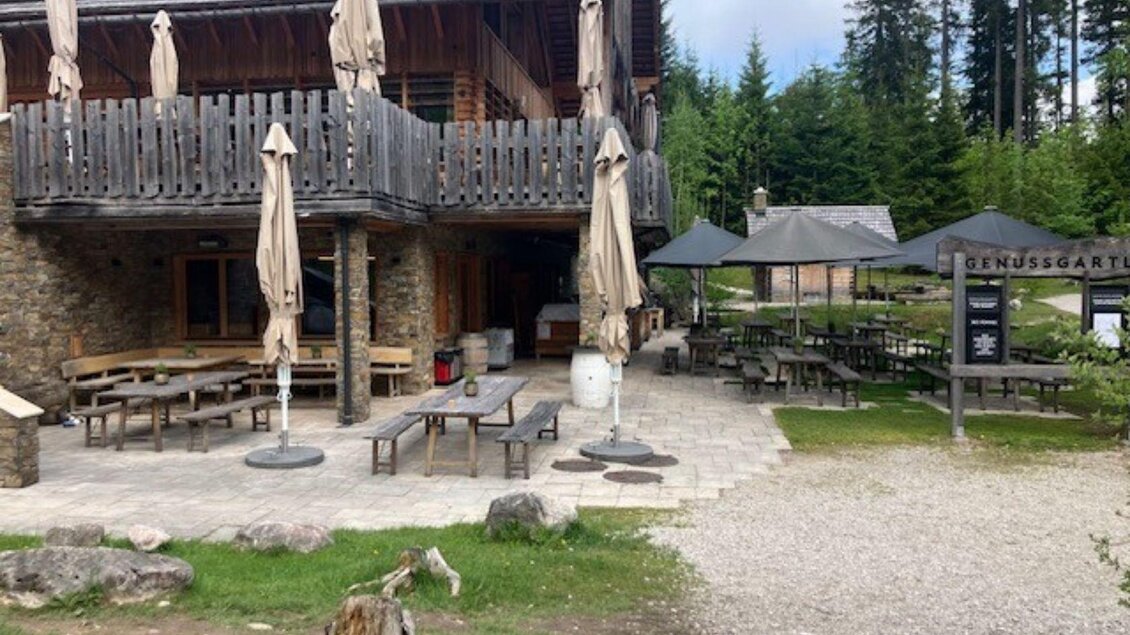 Der Eingang vom Genussladen unterhalb des Restaurants der Kohlröserlhütte, vor dem sich auch das Genuss Gartl befindet. Im Genuss Gartl davor stehen gemütliche Holzgarnituren und Sonnenschirme, und laden im Sommer zu einer Erfrischung umgeben von der Landschaft rund um den malerischen Ödensee ein. | © TVB Ausseerland Salzkammergut (c) Heike Temmel