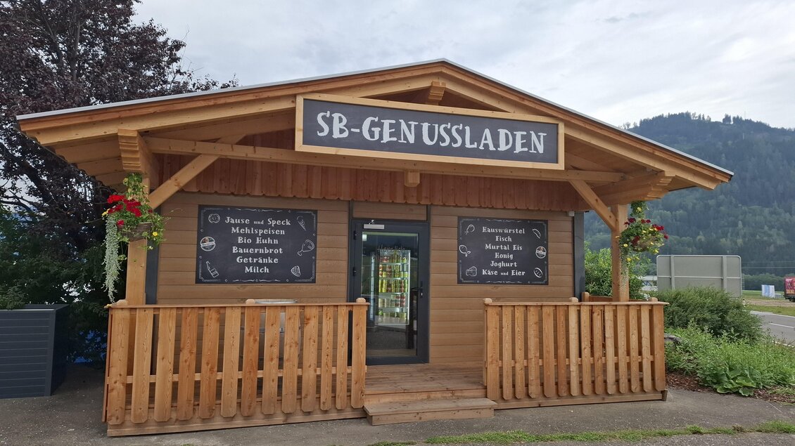 Ein kleines, hölzernes Geschäft mit der Aufschrift „SB-Genussladen“. Es ist von Pflanzen umgeben und liegt in einer ländlichen Umgebung. | © Erlebnisregion Murtal