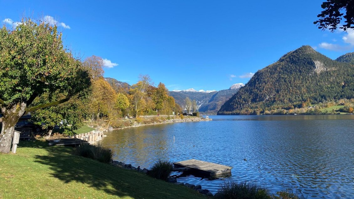 <p>Die ruhige Landschaft von Grundlsee im Ausseerland Salzkammergut mit dem klaren, gleichnamigen See und grünen Wiesen Richtung Ressen. Im Hintergrund sind die Ausläufer des Toten Gebirges und ein blauer Himmel sichtbar.</p> | © Bettina Scheck