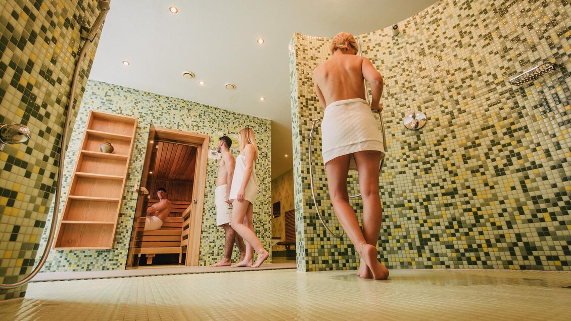 Ein moderner Wellnessbereich mit Fliesen in grünlichen Tönen. Zwei Frauen genießen ihre Zeit in der Sauna und Dusche. | © Stadtgemeinde Trofaiach