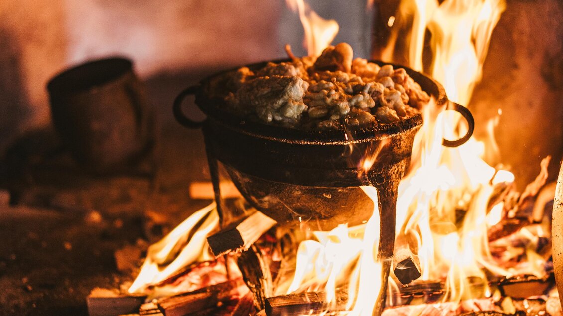 Ein traditioneller Holzofen mit loderndem Feuer und einem Kessel darauf. Umgeben von brennendem Holz und einem einfachen Pfannen. | © Oststeiermark Tourismus